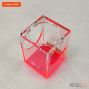 Neon pink acrylic cube pen holder with intersecting circular cutout windows, front angled view