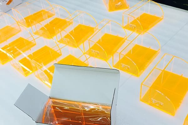 Rows of neon orange acrylic desk organizers laid out after production, with an individual retail box displayed alongside